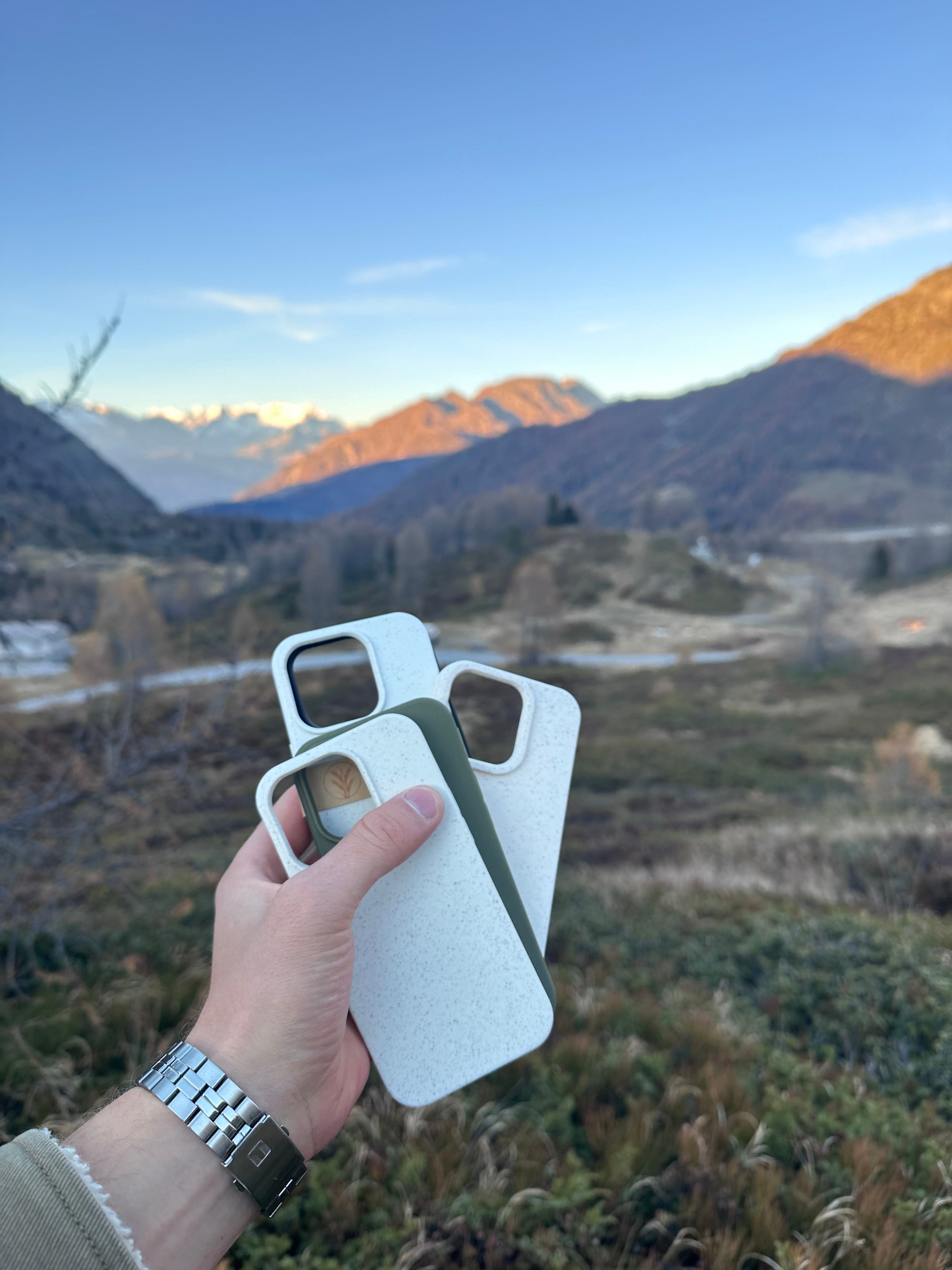 Zwei nachhaltige iPhone Hüllen in Weiß und Grün, gehalten in der Natur vor Berglandschaft